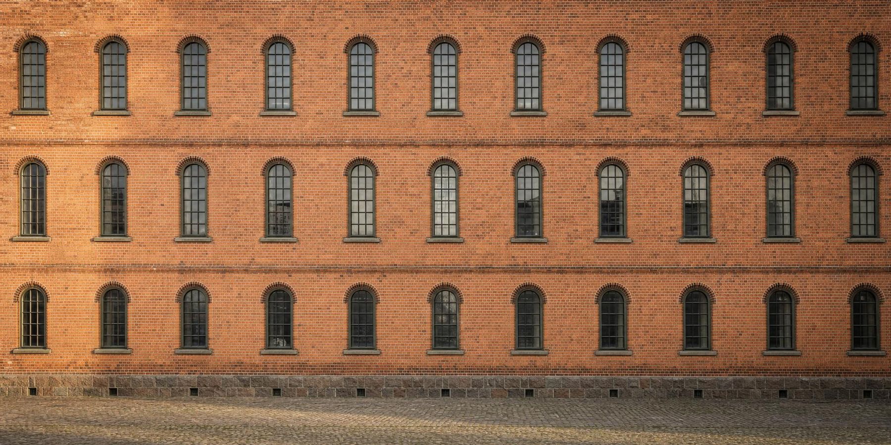 Backsteinfassade eines Speichergebäudes im Streiflicht des Morgens, gleichmäßige Reihen hoher Fenster