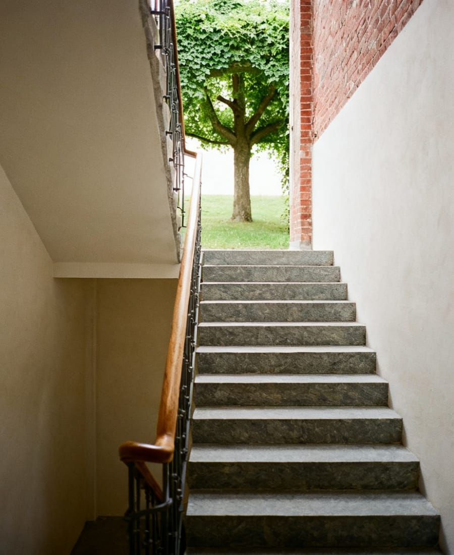 Treppenhaus mit Steinstufen und schmiedeeisernem Geländer, von oben einfallendes Tageslicht